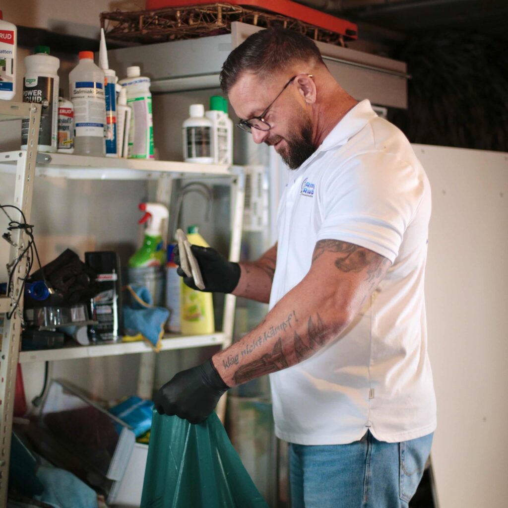 Person bei einer Aachener Entr&uuml;mpelung, die Sachen in einen M&uuml;llsack entsorgt