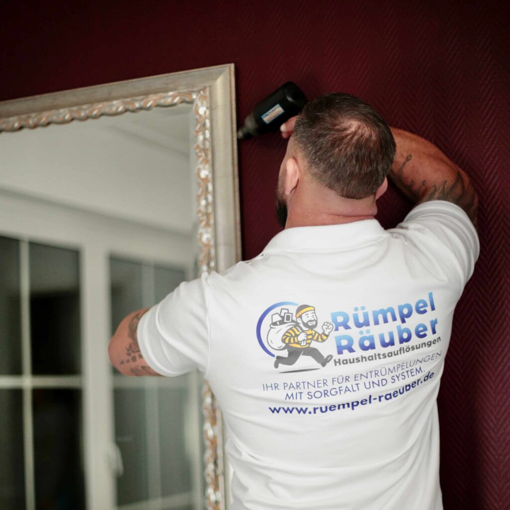 Mann mit Akkuschrauber bei Aachener Entr&uuml;mpelung der einen Spiegel demontiert